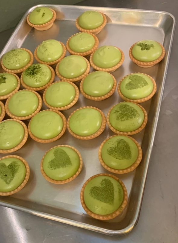 a tray filled with little circular Matcha-flavored cheese tart. Some have heart-shaped dusted over them.