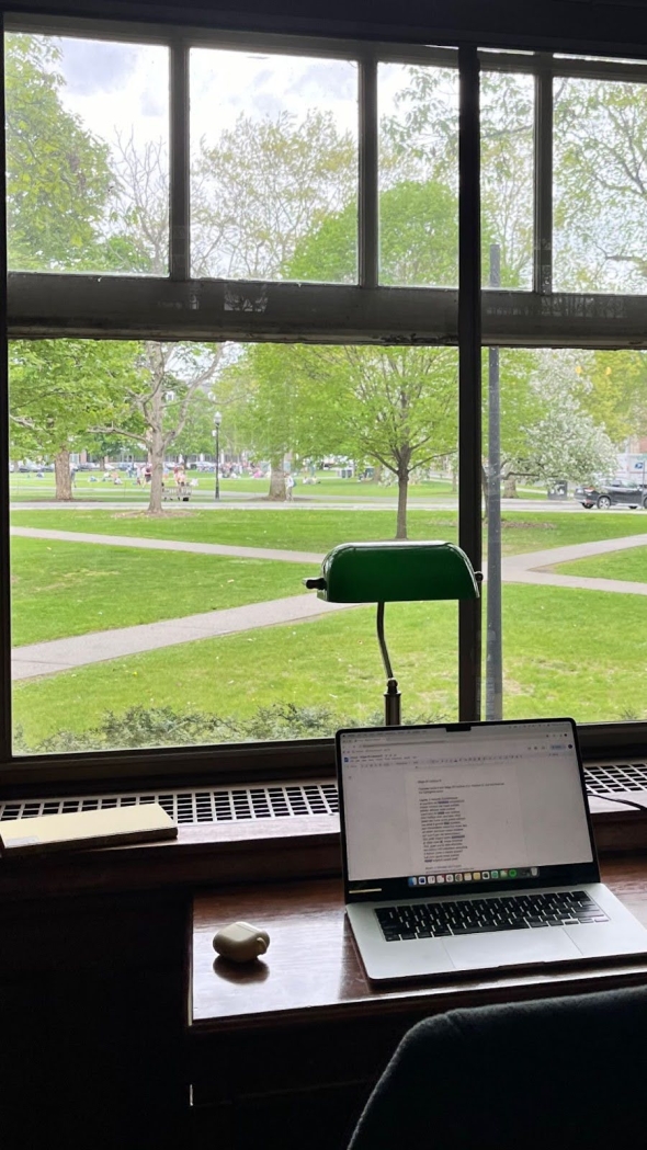 A laptop sitting on a desk at Sanborn Library. In the background, there is a window overlooking the Green.