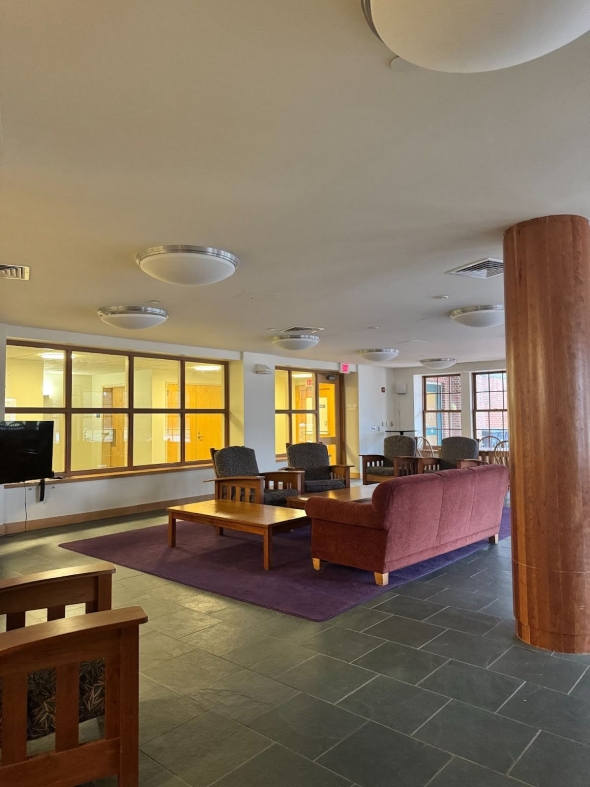 A large room with couches, arm chairs, and tables. There is a TV in the corner.