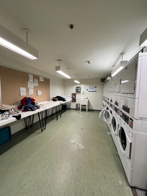 A laundry room, with a long folding table against one wall, a washtub, and washers and dryers lined up on the other wall.