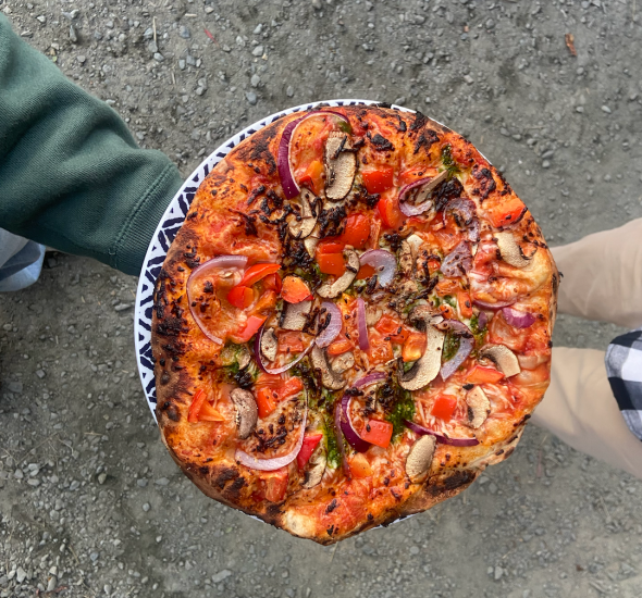 The pizza is the center of the image. The pizza is slightly charred, really orange-looking, and has black spots throughout