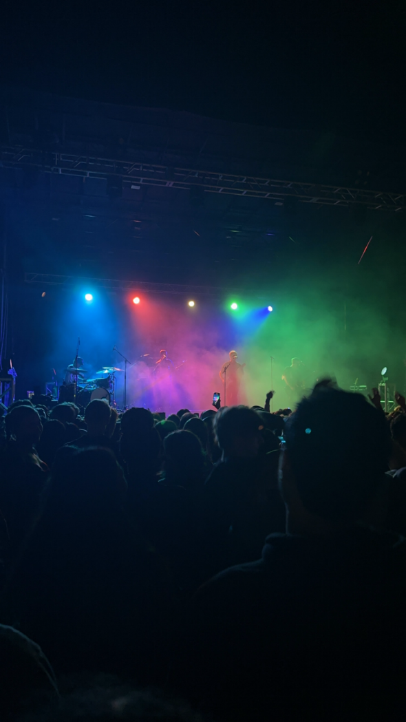 Concert with green, blue, and red lights with a band on stage and people in the crowd