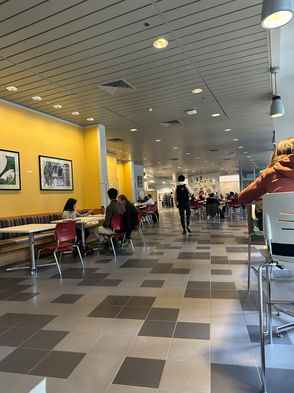 Cafe with checkered flooring and people sitting and talking as well as some people walking.