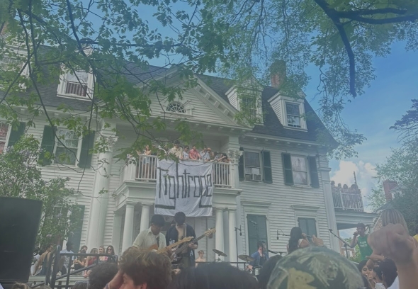 Student band performing with a crowd gathered around and some students watching from a balcony above.