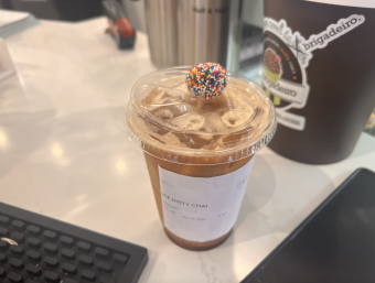 Coffee cup with a chocolate truffle covered in sprinkles on top of it.