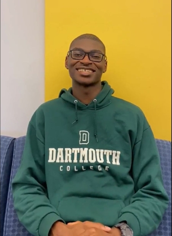 A picture of Denva Jr. sitting down and wearing a green Dartmouth hoodie. 