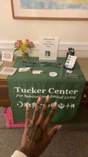 A picture of my hand with freshly drawn henna in front of the Tucker Center's welcome table. 