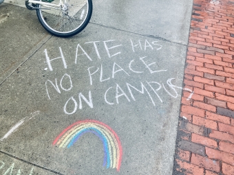 Chalk art that says "Hate has no place on campus" written in white, with a rainbow drawn underneath the words.