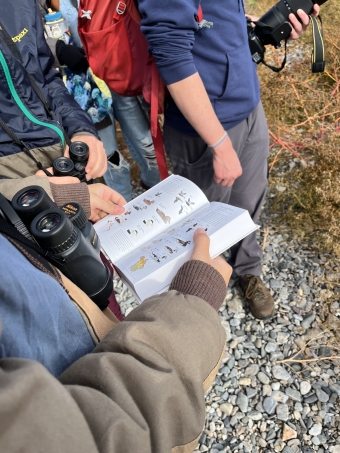 A photo of one of our trip members holding a field guide. In the background, other trip members are standing and looking at the guide.