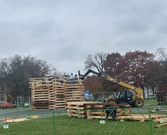 a forklift and the bonfire are in the middle of the green. The grey sky is above and the green grass is below.