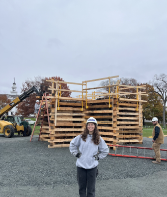 The picture shows Serena with her hands on her hips in front of the same bonfire. She is wearing a grey sweatshirt and there is the forklift machine behind her to the left.