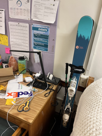skis are propped up against a wall. A desk with school supplies is to the right.