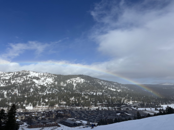 a blue sky with some white clouds and a rainbow arcing below it. A mountain is far away.