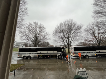 two dartmouth coach buses are lined next to each other. In front of them is the sidewalk wet with rain.