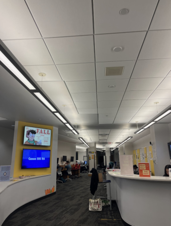 a picture of the library with two tvs on the left wall and grey desks on the left and right.